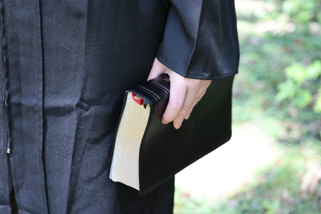 Person in a black graduation gown holding a ceremonial sword at their side. DMIN Resources