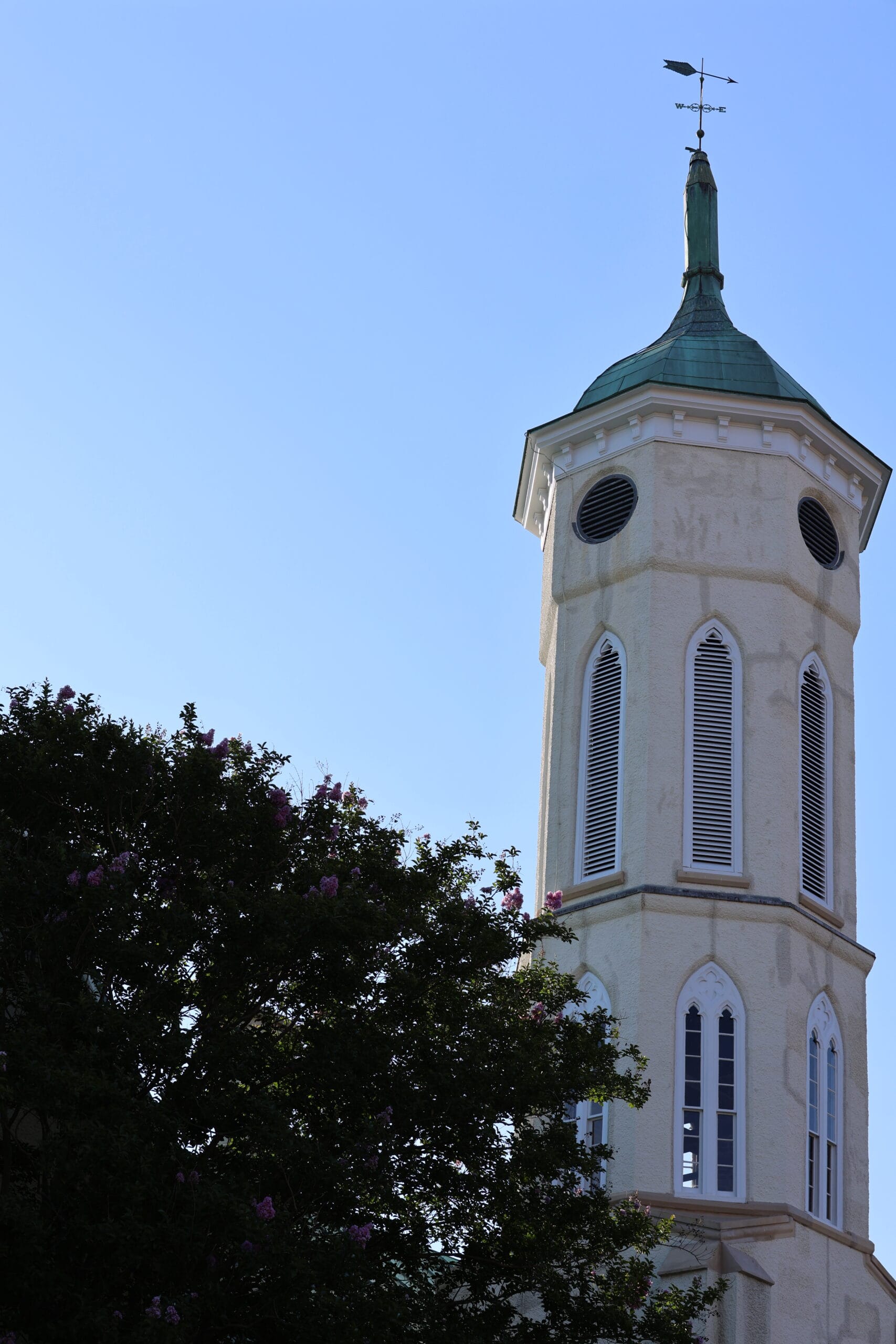 Church steeple with a green copper roof rising above a leafy tree against a clear blue sky, weather vane at the peak. Faculty & Staff